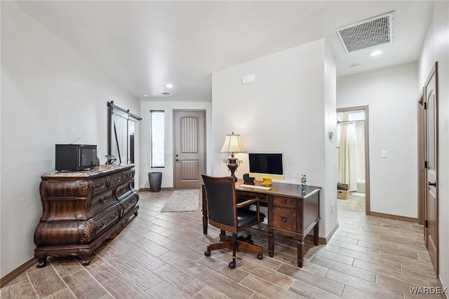 office area featuring a barn door, wood tiled floor, visible vents, and baseboards