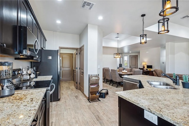 kitchen with appliances with stainless steel finishes, open floor plan, a sink, and hanging light fixtures