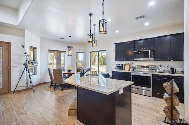 kitchen featuring a breakfast bar area, stainless steel appliances, visible vents, an island with sink, and decorative light fixtures