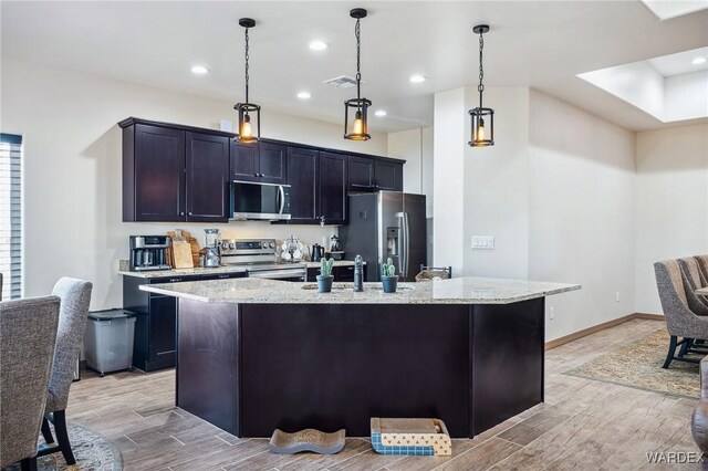 kitchen with an island with sink, pendant lighting, and stainless steel appliances