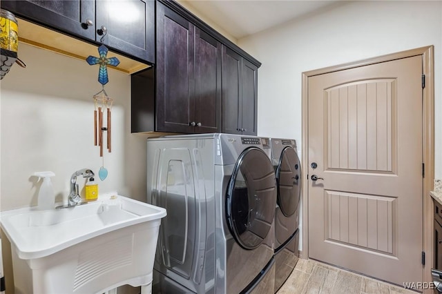 clothes washing area with washer and dryer, cabinet space, a sink, and light wood finished floors