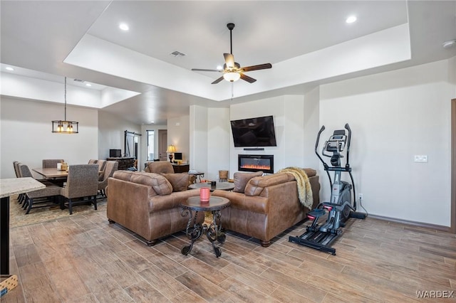 living room with a raised ceiling, a glass covered fireplace, and wood finish floors