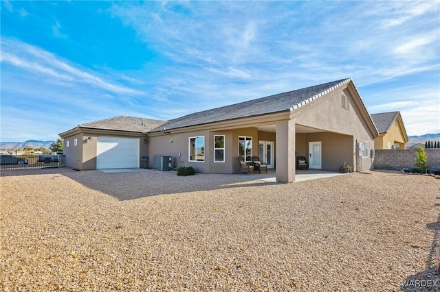 rear view of property with stucco siding, a mountain view, fence, a garage, and cooling unit