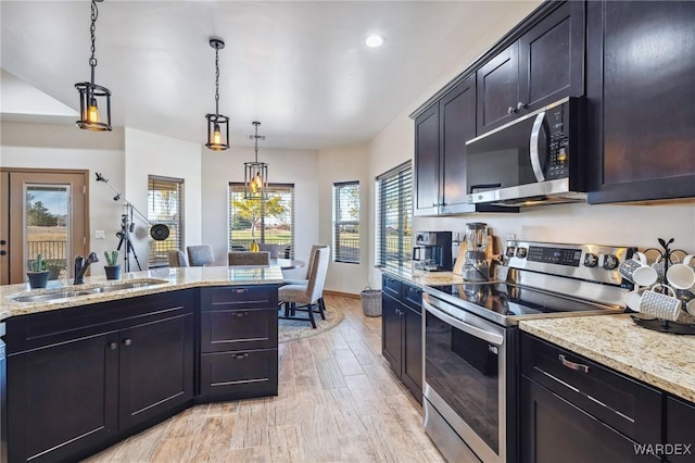 kitchen featuring hanging light fixtures, appliances with stainless steel finishes, a sink, and light stone counters