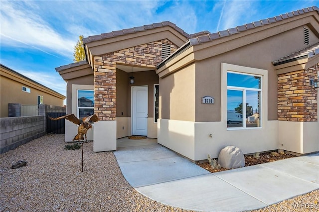 view of exterior entry featuring stone siding, fence, a patio, and stucco siding