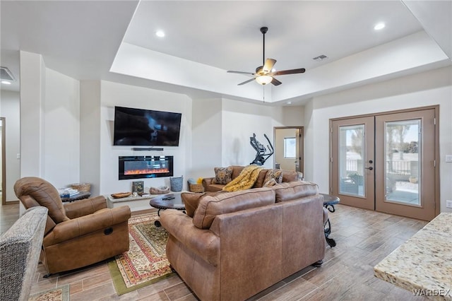 living area with wood tiled floor, a tray ceiling, french doors, and a glass covered fireplace