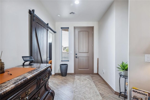 entrance foyer featuring wood tiled floor, visible vents, baseboards, and a barn door