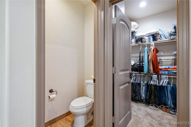 bathroom featuring a walk in closet, toilet, and baseboards