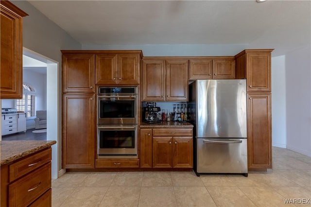 kitchen featuring stainless steel appliances, brown cabinets, dark stone countertops, and light tile patterned floors