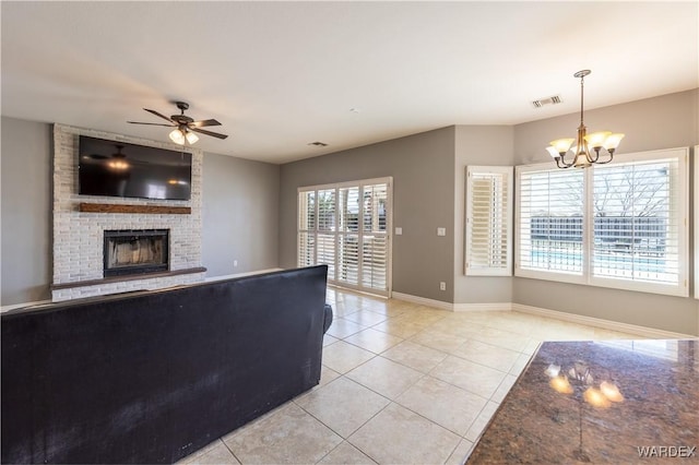 unfurnished living room with a fireplace, light tile patterned floors, visible vents, baseboards, and ceiling fan with notable chandelier