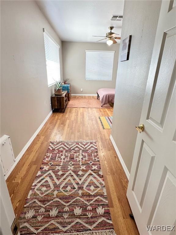 hall featuring visible vents, baseboards, and wood finished floors