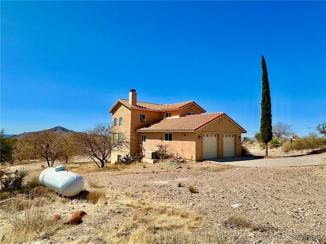 view of side of home featuring a tile roof, a chimney, stucco siding, a garage, and driveway