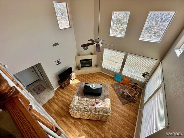 living area with a high ceiling, a tiled fireplace, a ceiling fan, wood finished floors, and baseboards