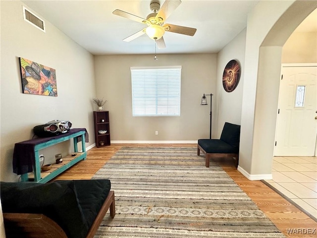 sitting room with visible vents, arched walkways, baseboards, ceiling fan, and light wood-style floors