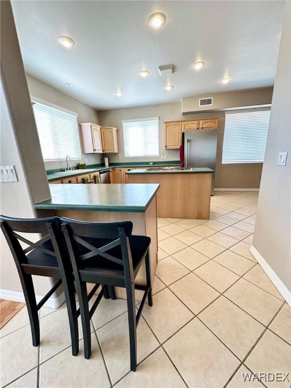 kitchen featuring light tile patterned floors, a peninsula, stainless steel appliances, light brown cabinetry, and dark countertops