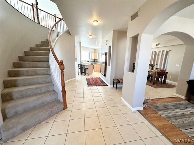 foyer entrance with light tile patterned floors, arched walkways, visible vents, baseboards, and stairs