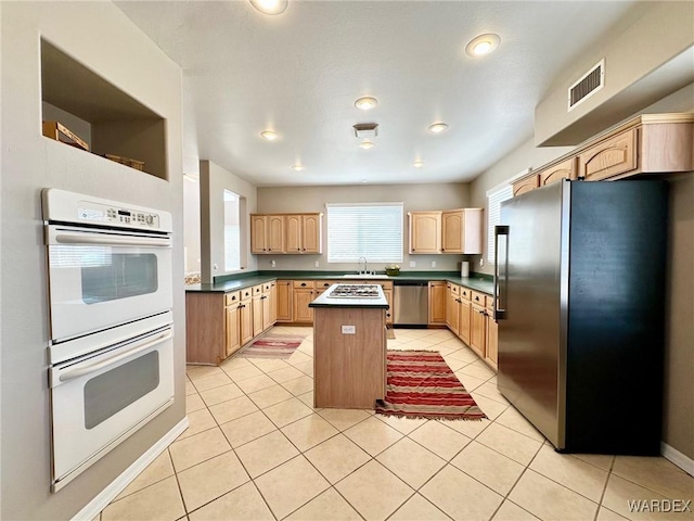 kitchen featuring light tile patterned floors, a kitchen island, stainless steel appliances, light brown cabinets, and a sink