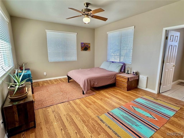 bedroom with light wood-style flooring, multiple windows, baseboards, and a ceiling fan