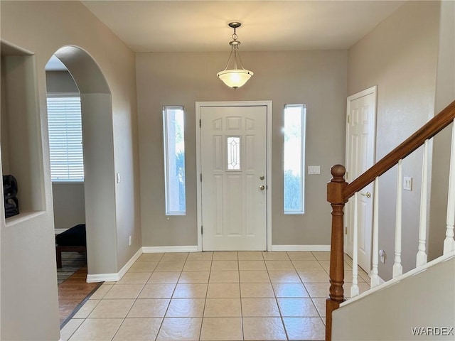 entrance foyer with light tile patterned floors, arched walkways, stairs, and baseboards