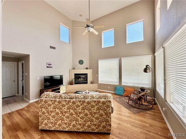 living area featuring baseboards, visible vents, a tiled fireplace, light wood-style flooring, and ceiling fan