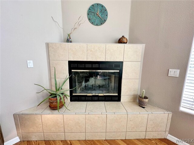 living area with ceiling fan, light wood finished floors, a tiled fireplace, and baseboards