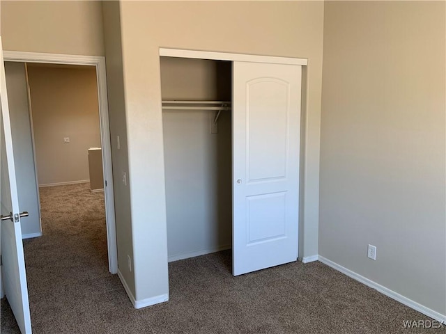 unfurnished bedroom featuring dark colored carpet, a closet, and baseboards