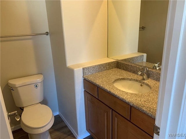 bathroom with toilet, wood finished floors, vanity, and baseboards