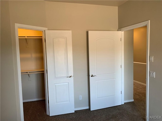 unfurnished bedroom with dark colored carpet, a closet, and baseboards