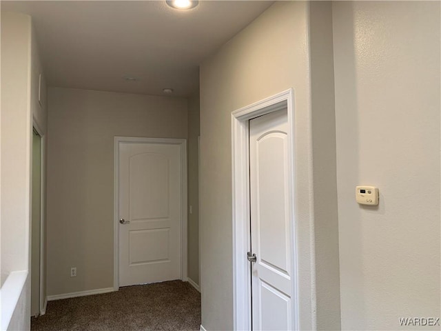 hall with dark colored carpet and baseboards