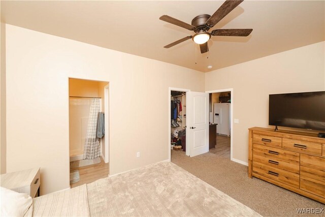 bedroom featuring white refrigerator with ice dispenser, a closet, light colored carpet, a spacious closet, and connected bathroom