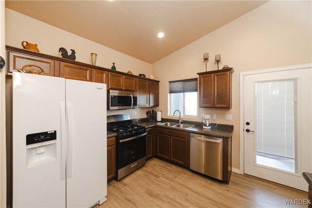 kitchen featuring light wood-style flooring, stainless steel appliances, a sink, vaulted ceiling, and dark countertops