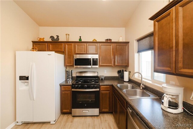 kitchen with appliances with stainless steel finishes, dark countertops, a sink, and brown cabinets