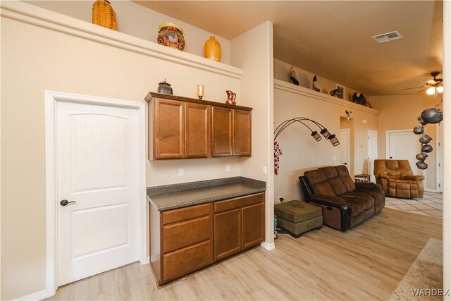 kitchen featuring visible vents, brown cabinetry, dark countertops, open floor plan, and light wood-type flooring