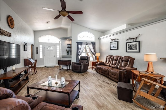 living area featuring visible vents, arched walkways, a ceiling fan, light wood-style floors, and high vaulted ceiling