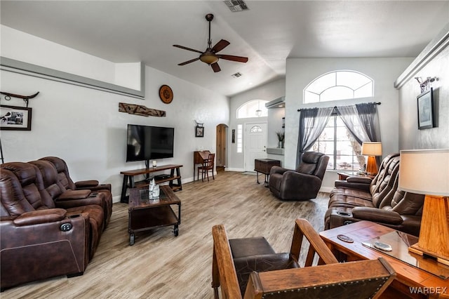 living room with arched walkways, ceiling fan, light wood-style flooring, visible vents, and vaulted ceiling