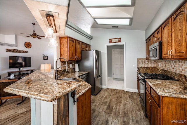 kitchen featuring stainless steel appliances, brown cabinetry, a sink, and light stone countertops