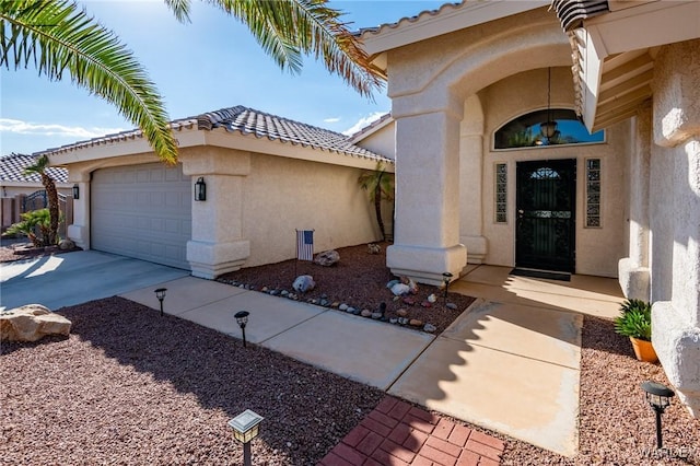 entrance to property featuring a garage, driveway, a tiled roof, and stucco siding