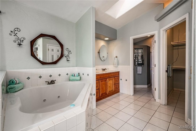 bathroom with a walk in closet, lofted ceiling with skylight, vanity, tile patterned flooring, and a tub with jets