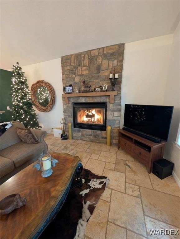 living area featuring stone tile flooring, a stone fireplace, and baseboards