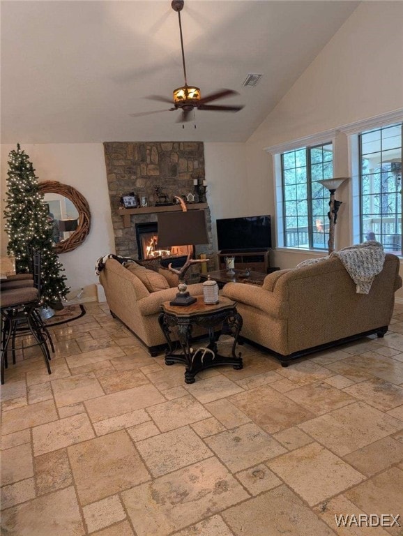 living room with a ceiling fan, lofted ceiling, visible vents, and a stone fireplace