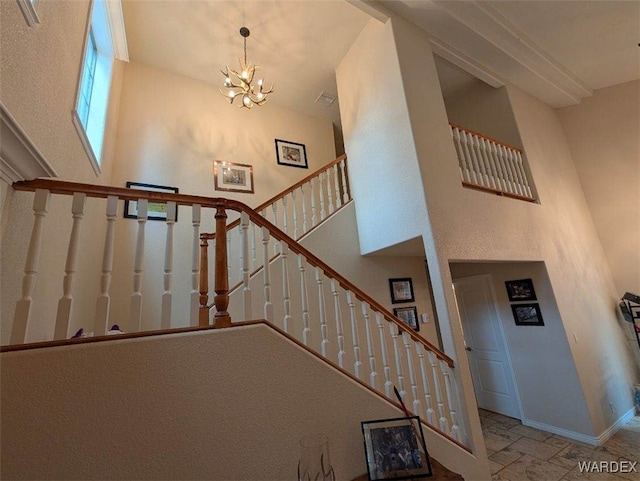 stairs with a chandelier, stone finish floor, a towering ceiling, and baseboards