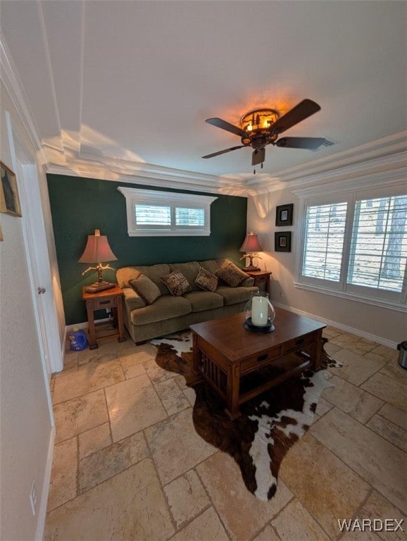 living area with baseboards, crown molding, stone tile floors, and ceiling fan