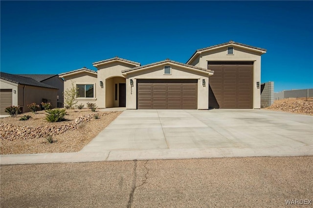 mediterranean / spanish house with a garage, driveway, a tiled roof, and stucco siding