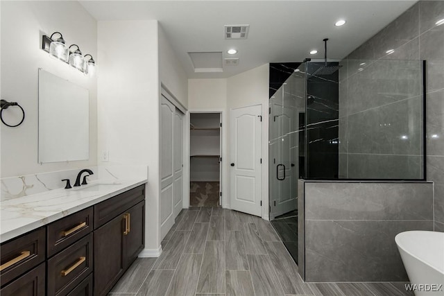 full bath with visible vents, a spacious closet, a shower stall, vanity, and a freestanding tub