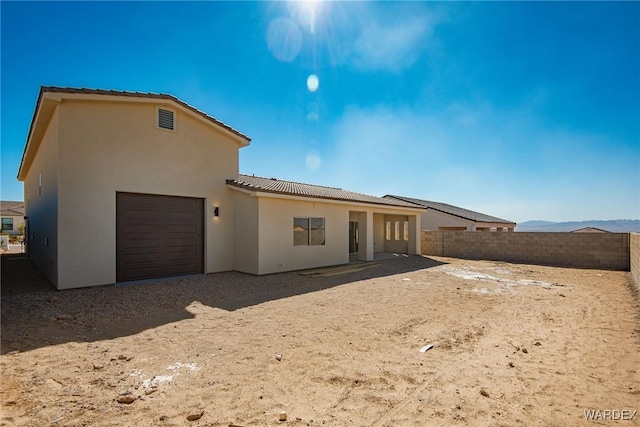 back of house featuring a fenced backyard, a tiled roof, a mountain view, and stucco siding