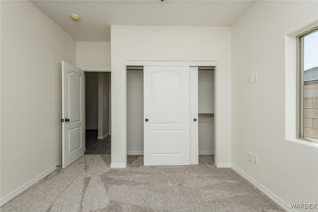 unfurnished bedroom with a closet, light colored carpet, and baseboards