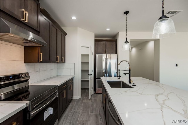 kitchen featuring under cabinet range hood, a sink, hanging light fixtures, appliances with stainless steel finishes, and light stone countertops