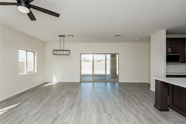 interior space featuring light wood-style flooring, a healthy amount of sunlight, visible vents, and baseboards