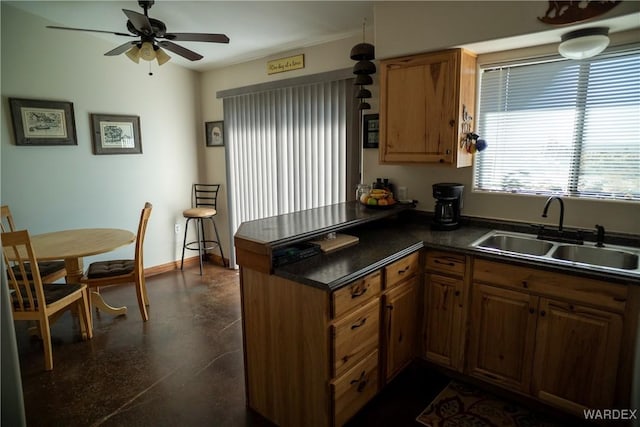 kitchen featuring a peninsula, a sink, baseboards, brown cabinetry, and dark countertops