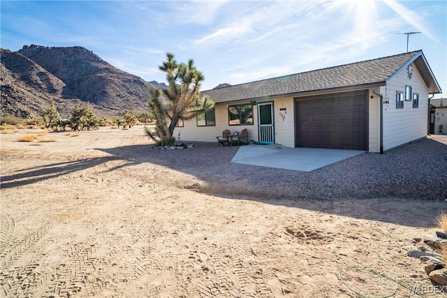 ranch-style home with a garage, a mountain view, driveway, and a shingled roof